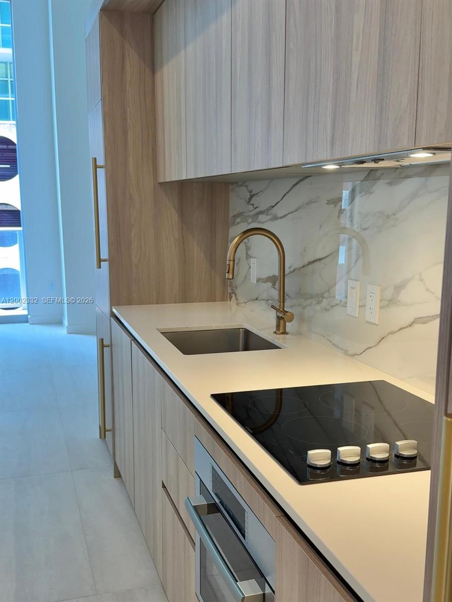 A modern kitchen features light wood cabinetry, a marble backsplash, and a gold faucet — 77 SE 5th street # 1010, Miami FL 33131, MIAMI, FL