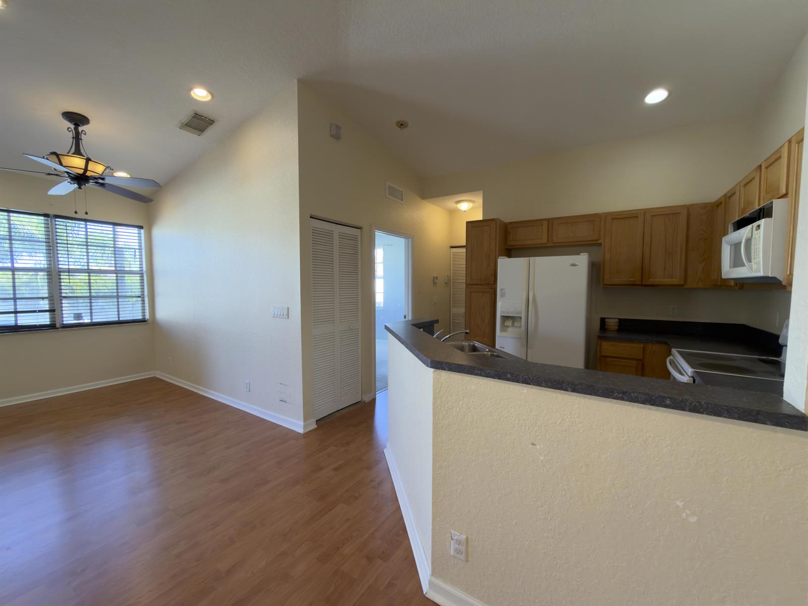 An open-concept kitchen with wood cabinets and a breakfast bar overlooks a living area — 1712 Carvelle Drive, Riviera Beach FL 33404, RIVIERA BEACH, FL