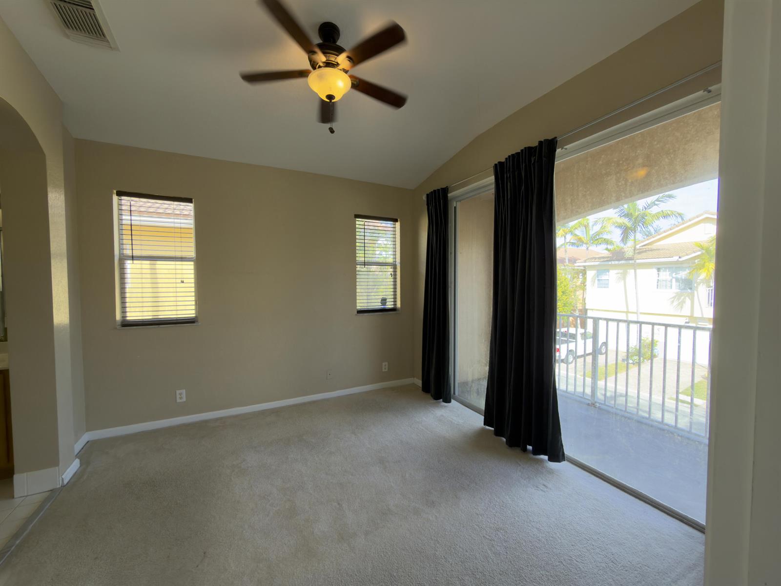 An empty bedroom features beige carpet, two windows with blinds, and a sliding glass door — 1712 Carvelle Drive, Riviera Beach FL 33404, RIVIERA BEACH, FL