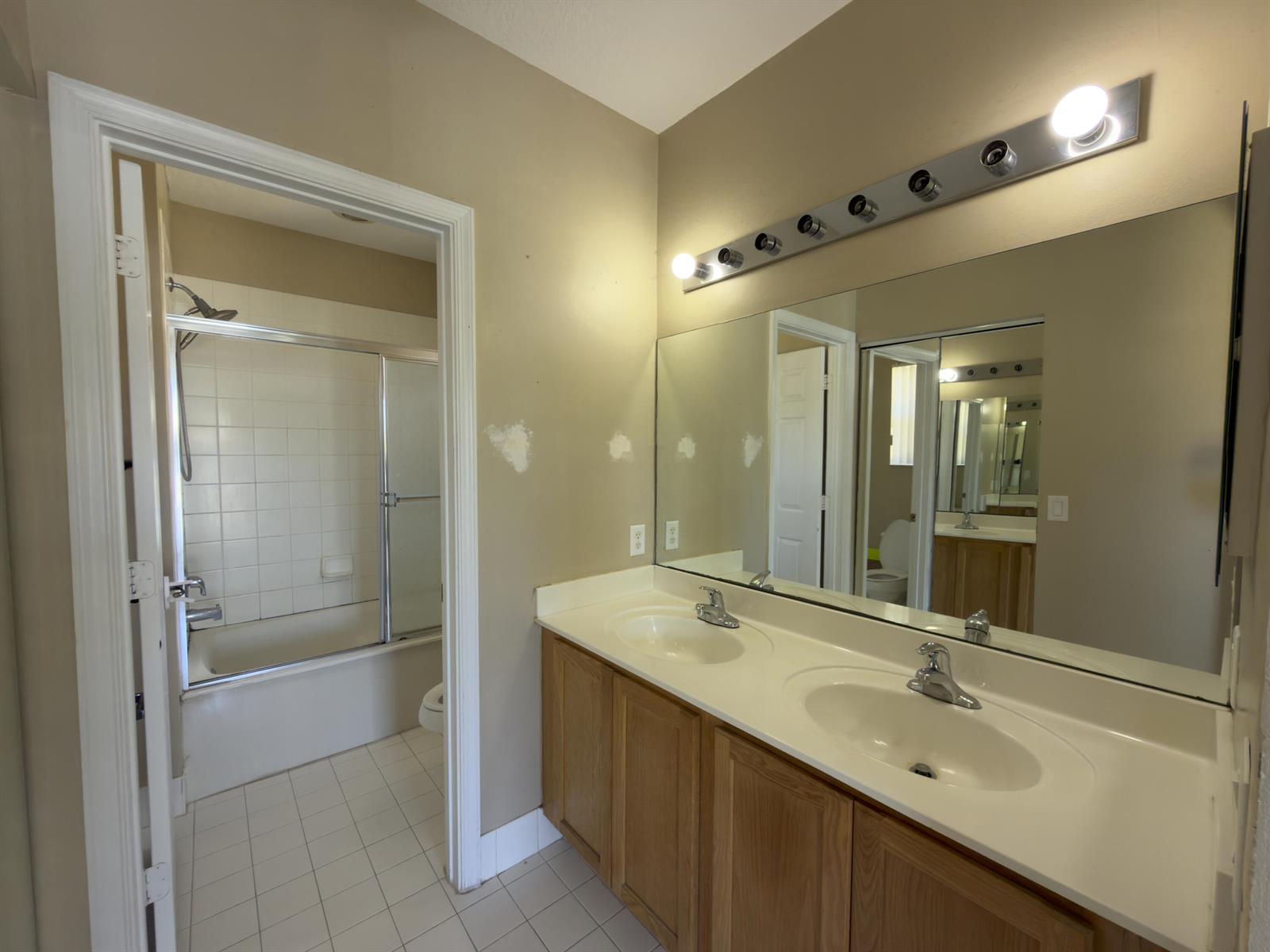 A bathroom with a double vanity, wood cabinets, a large mirror, and a shower-tub combo — 1712 Carvelle Drive, Riviera Beach FL 33404, RIVIERA BEACH, FL