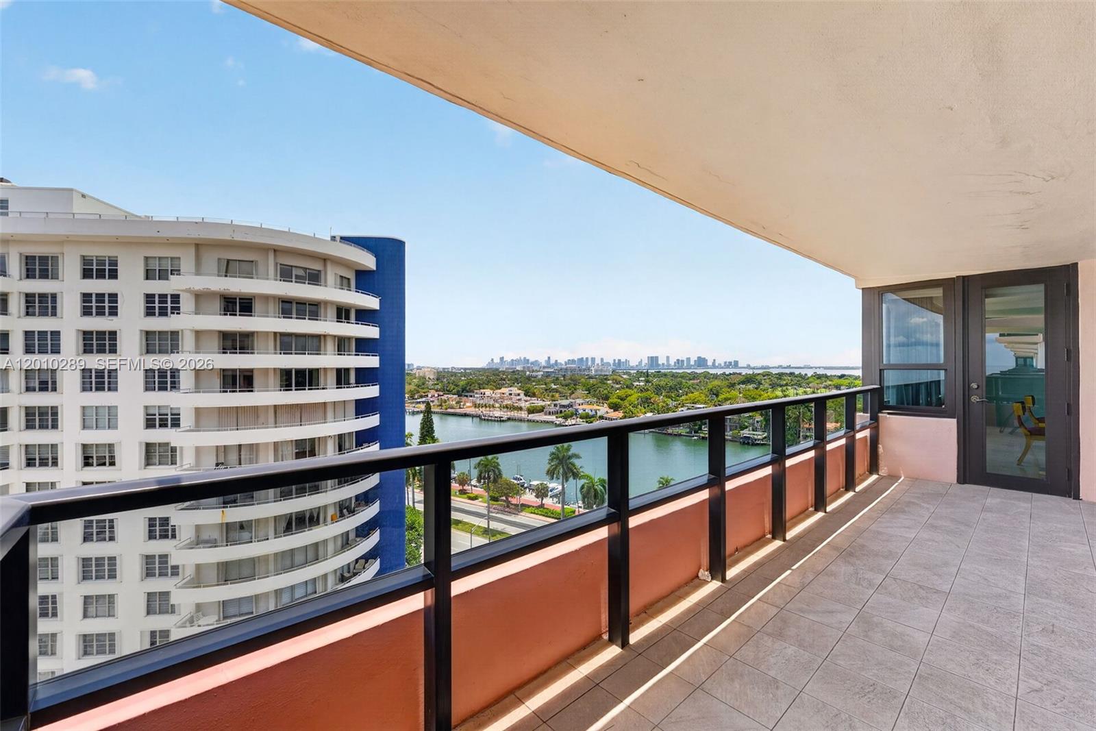 A balcony with tiled flooring, black railings, and a view of a waterway and city — 5225 Collins Ave # 1519, Miami Beach FL 33140, MIAMI BEACH, FL