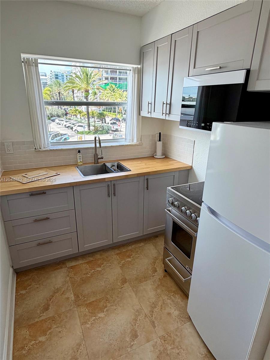 A kitchen features gray cabinets, a wooden countertop, a stainless steel sink, and a window — 9248 Collins Ave # 205, Surfside FL 33154, SURFSIDE, FL
