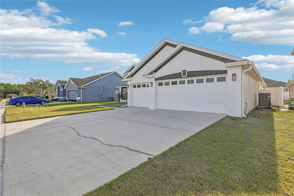 A white single-story house with a three-car garage and a cracked concrete driveway — 4612 HURON BAY CIRCLE, KISSIMMEE, FL