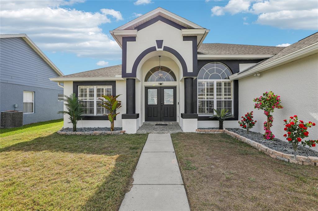 A front view of a single-story house with a white stucco facade and dark trim — 4612 HURON BAY CIRCLE, KISSIMMEE, FL