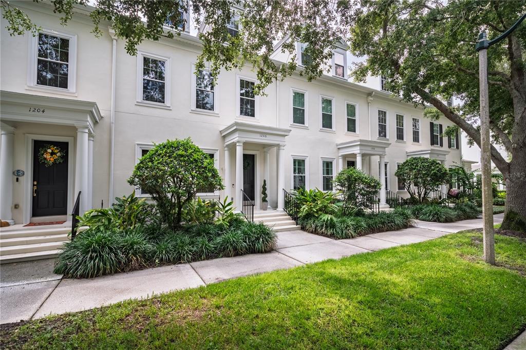 A row of white townhouses with black doors and green landscaping along a sidewalk — 1206 CELEBRATION AVENUE, CELEBRATION, FL