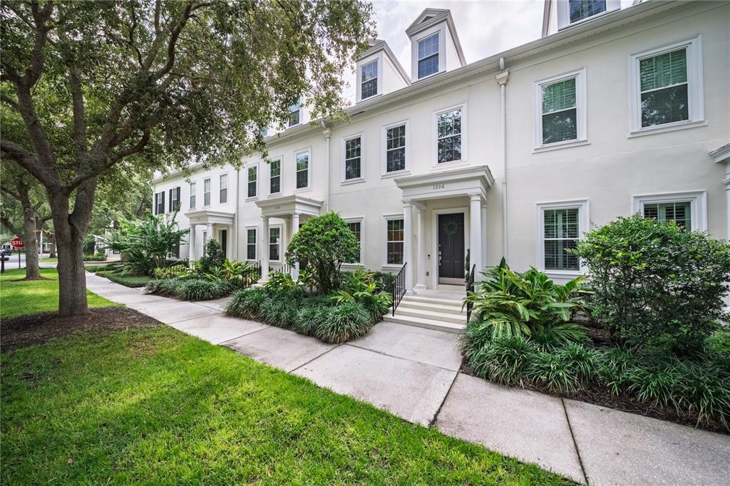 A row of white townhouses with dark doors and green landscaping along a sidewalk — 1206 CELEBRATION AVENUE, CELEBRATION, FL