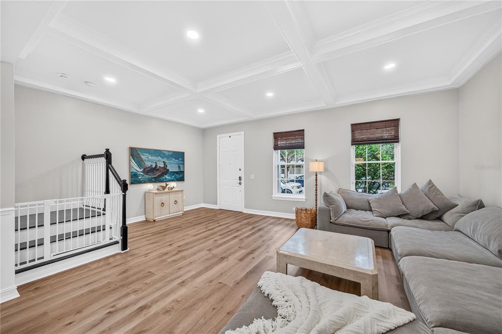 A living room with light wood floors, a coffered ceiling, and a large gray sectional sofa — 1206 CELEBRATION AVENUE, CELEBRATION, FL