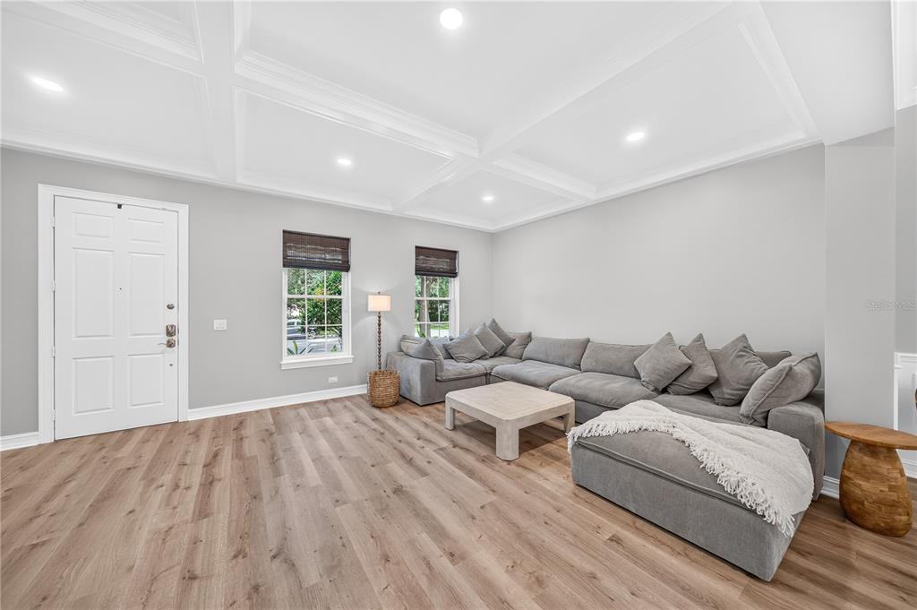A living room features light wood flooring, a coffered ceiling, and a large gray sectional sofa — 1206 CELEBRATION AVENUE, CELEBRATION, FL