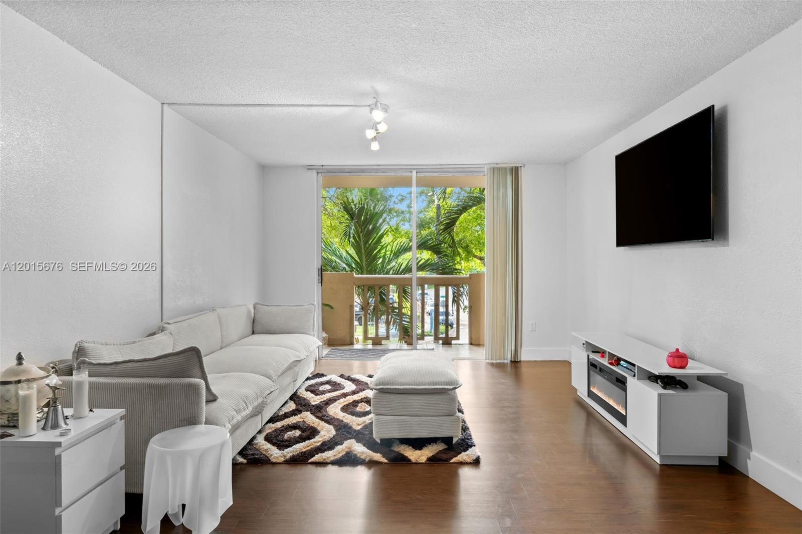 A living room features a white sofa, patterned rug, media console, and a balcony view — 1800 Sans Souci # 332, North Miami FL 33181, NORTH MIAMI, FL