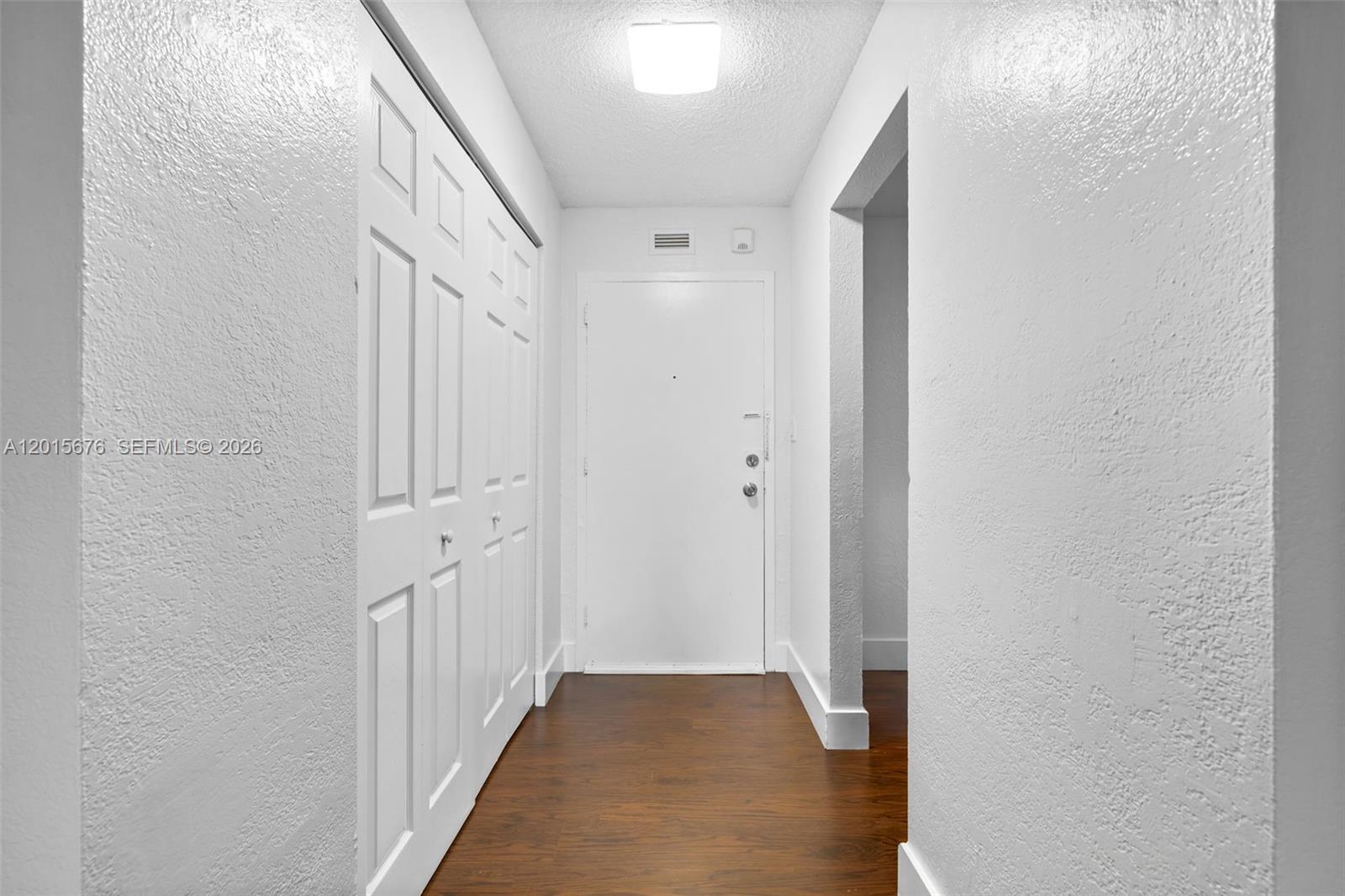 A white hallway features a closet with folding doors, a front door, and wood flooring — 1800 Sans Souci # 332, North Miami FL 33181, NORTH MIAMI, FL