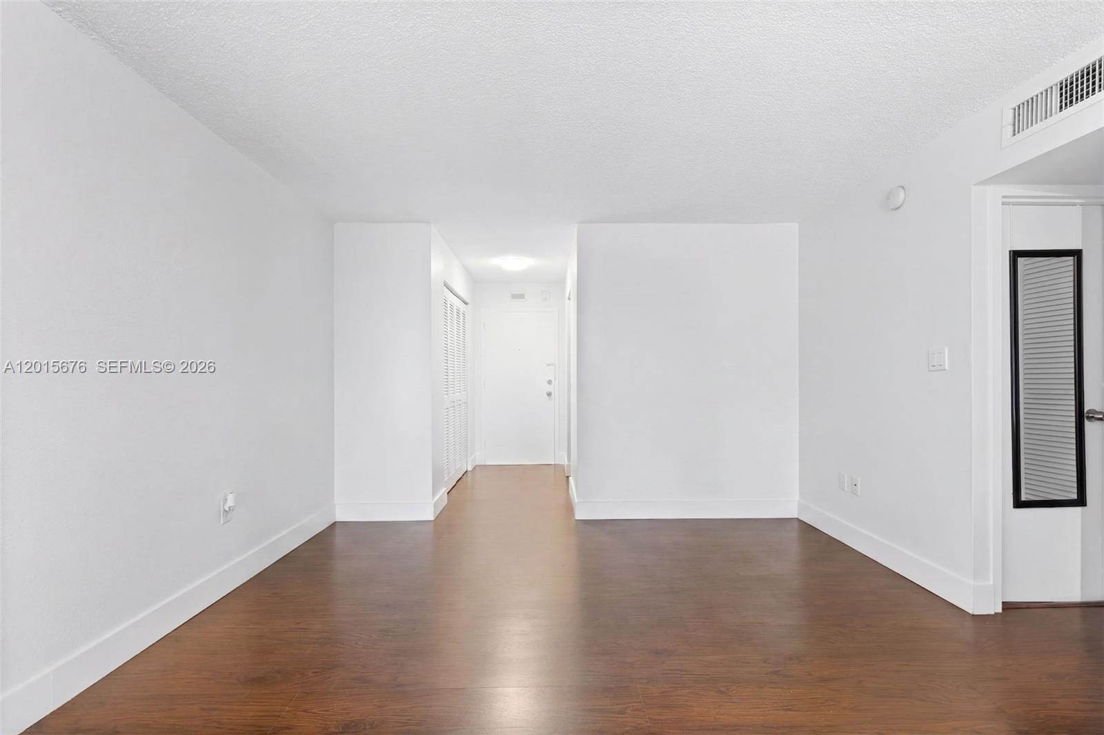 An empty room features white walls, dark wood-look flooring, and a white entry door — 1800 Sans Souci # 332, North Miami FL 33181, NORTH MIAMI, FL
