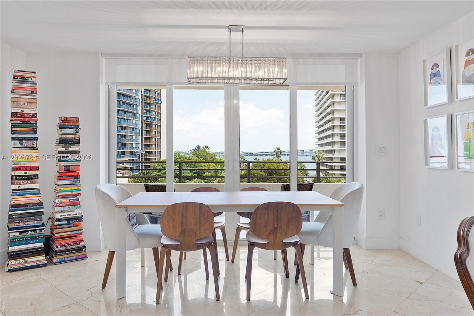 A dining room features a modern table, six chairs, two tall book stacks, and balcony views — 151 SE 15th Rd # 601, Miami FL 33129, MIAMI, FL