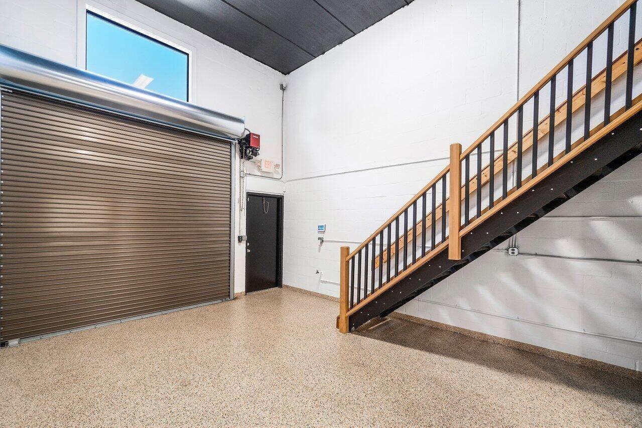 An industrial-style garage space features a roll-up door, a staircase, and epoxy flooring — 1771 Blount Road # 209, Pompano Beach FL 33069, POMPANO BEACH, FL