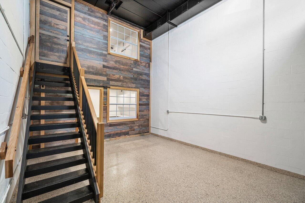 A room with a staircase, wood-paneled wall, two windows, and a white concrete wall — 1771 Blount Road # 209, Pompano Beach FL 33069, POMPANO BEACH, FL