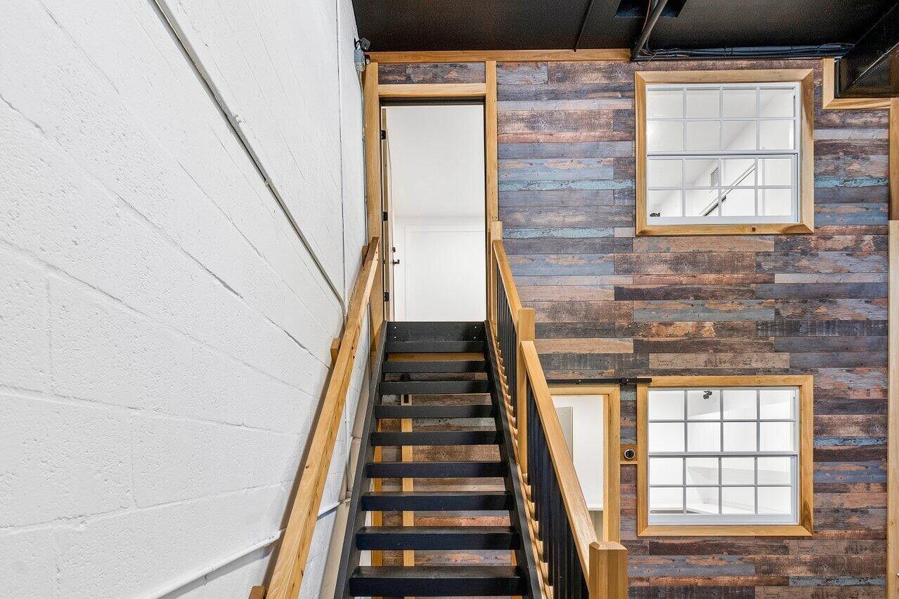 A staircase with black metal steps and wooden railings leads to a doorway against rustic wood-paneled walls — 1771 Blount Road # 209, Pompano Beach FL 33069, POMPANO BEACH, FL