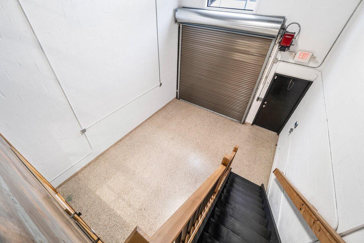 An elevated view of a garage interior with a roll-up door, stairs, and epoxy flooring — 1771 Blount Road # 209, Pompano Beach FL 33069, POMPANO BEACH, FL