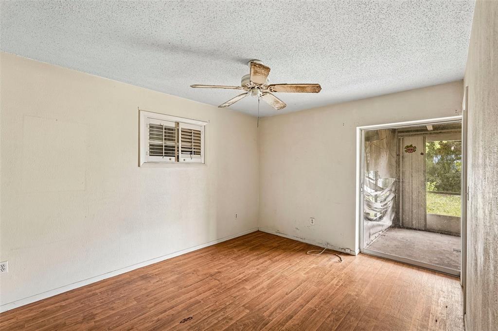 An empty room features wood-look flooring, a ceiling fan, a small window, and sliding doors — 838 CORDELE AVENUE NW, PORT CHARLOTTE, FL