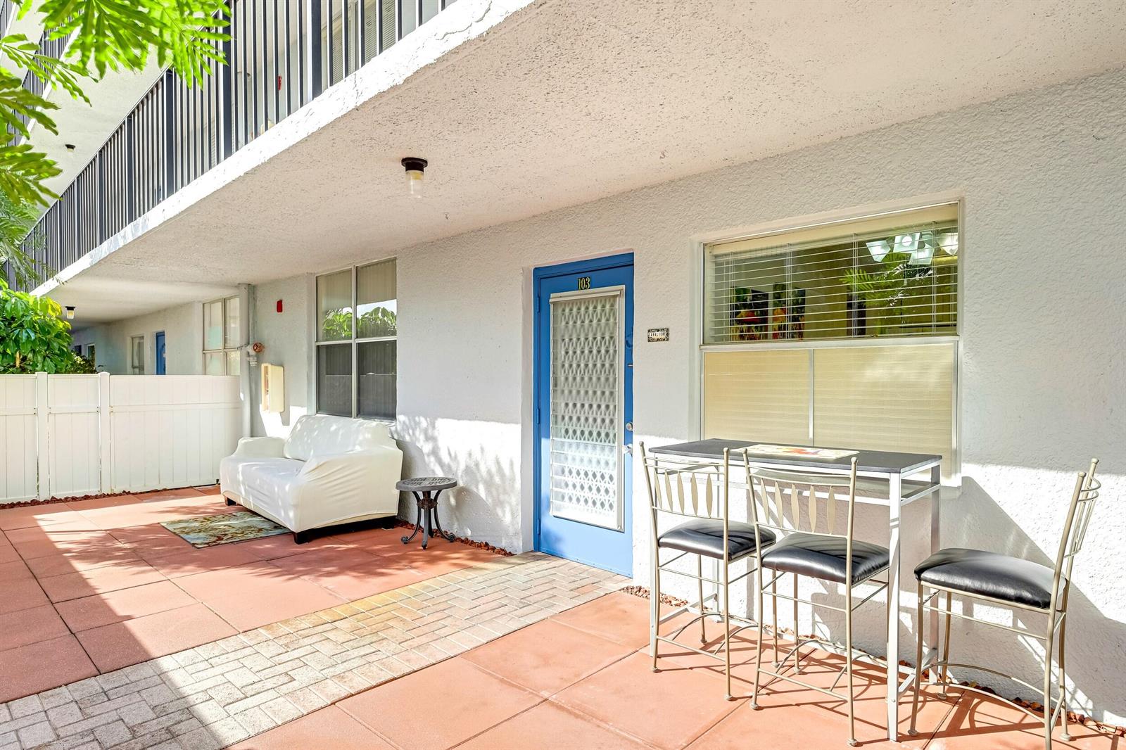 A patio area features a white sofa, a metal dining set, and a blue front door — 6650 S Oriole Boulevard # 1030, Delray Beach FL 33446, DELRAY BEACH, FL