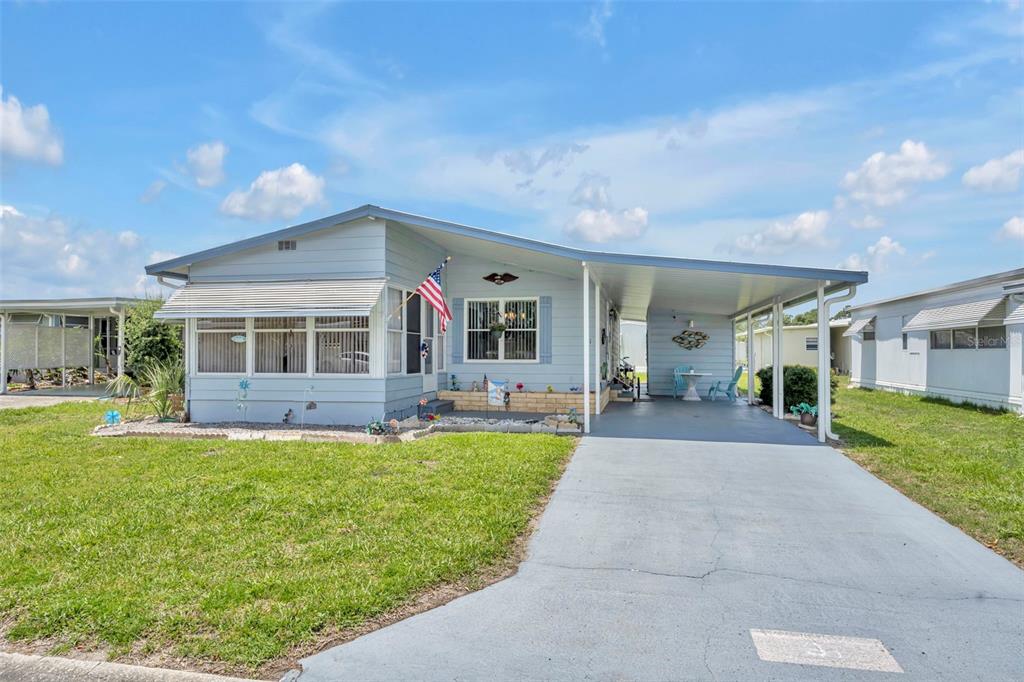 A light blue single-wide mobile home features a screened-in porch and an attached carport — 91 MAUNA LOA DRIVE, LEESBURG, FL