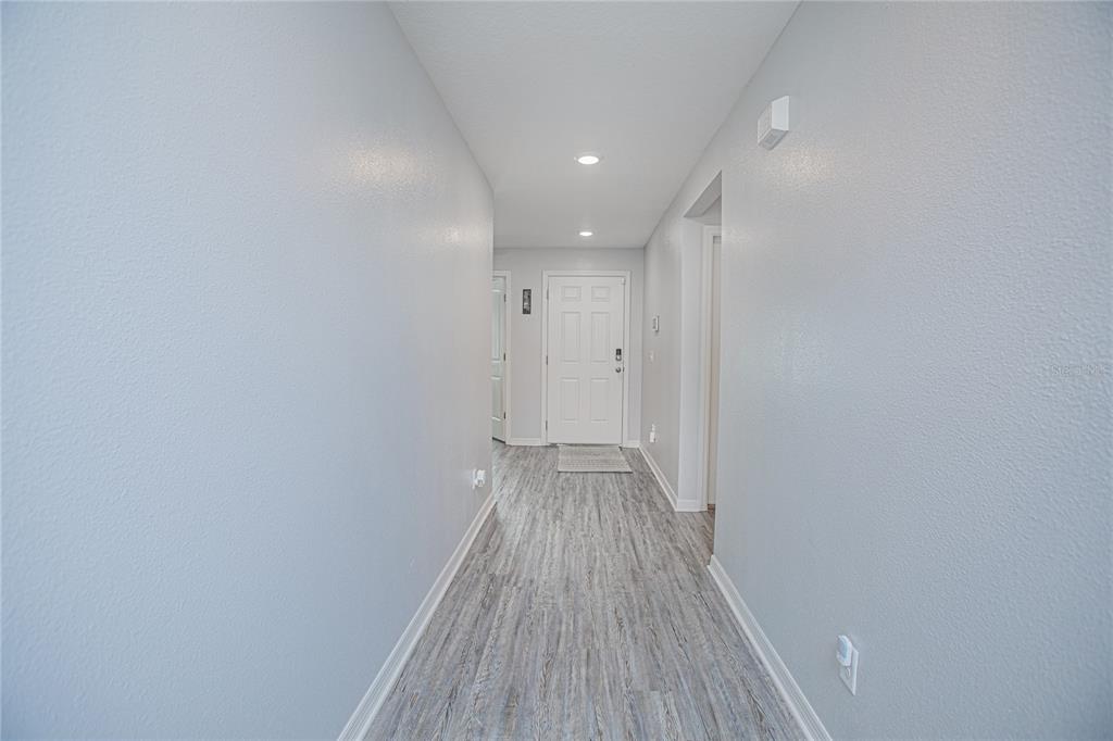 A hallway with light gray walls, wood-look flooring, and a white front door — 214 LINDA LANE, AUBURNDALE, FL