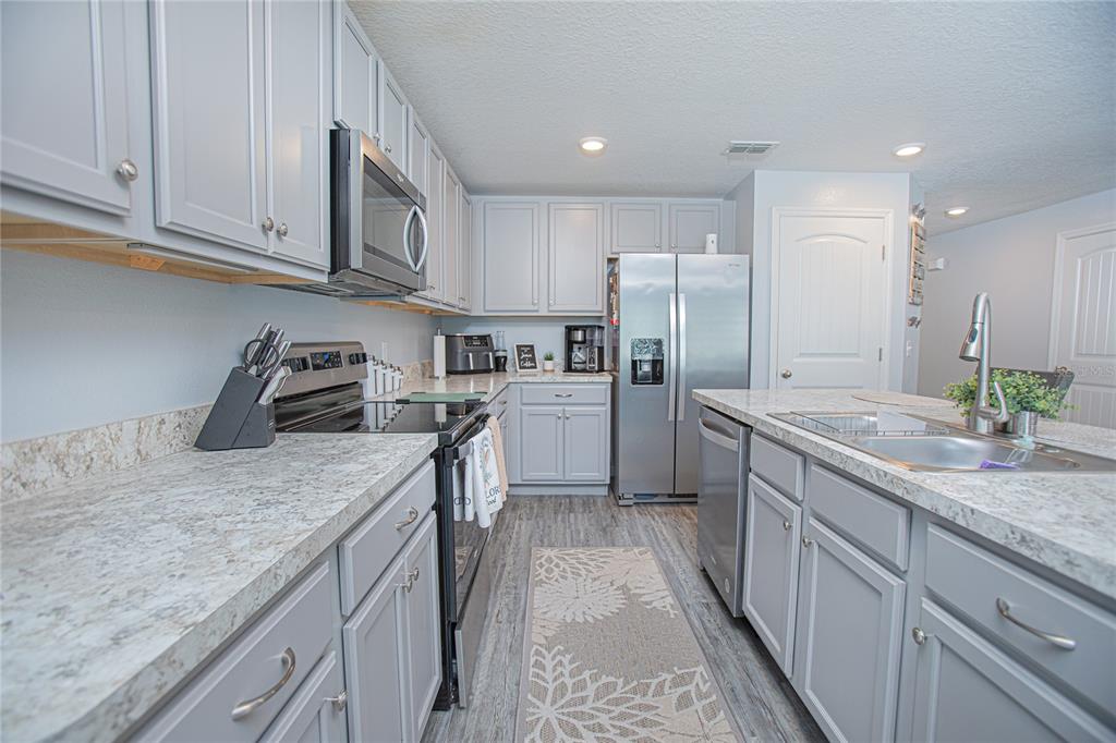 A kitchen features gray cabinets, stainless steel appliances, and light-colored granite countertops — 214 LINDA LANE, AUBURNDALE, FL