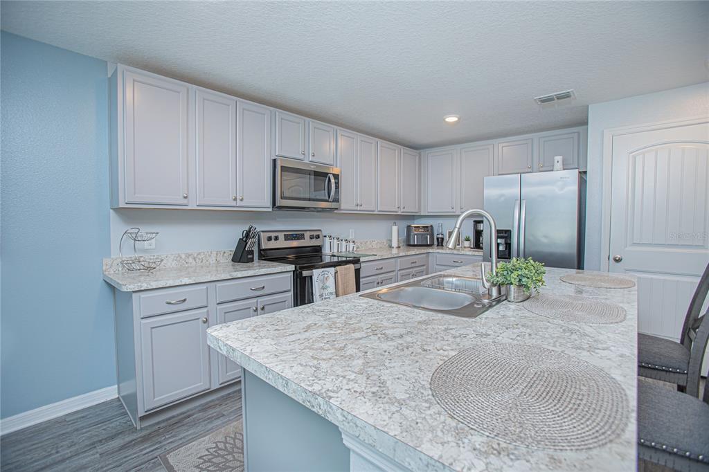 A kitchen features light gray cabinets, granite countertops, stainless steel appliances, and a central island — 214 LINDA LANE, AUBURNDALE, FL
