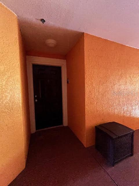 A dark front door is set into an orange textured wall on a covered porch — 5447 VINELAND ROAD UNIT 1210, ORLANDO, FL