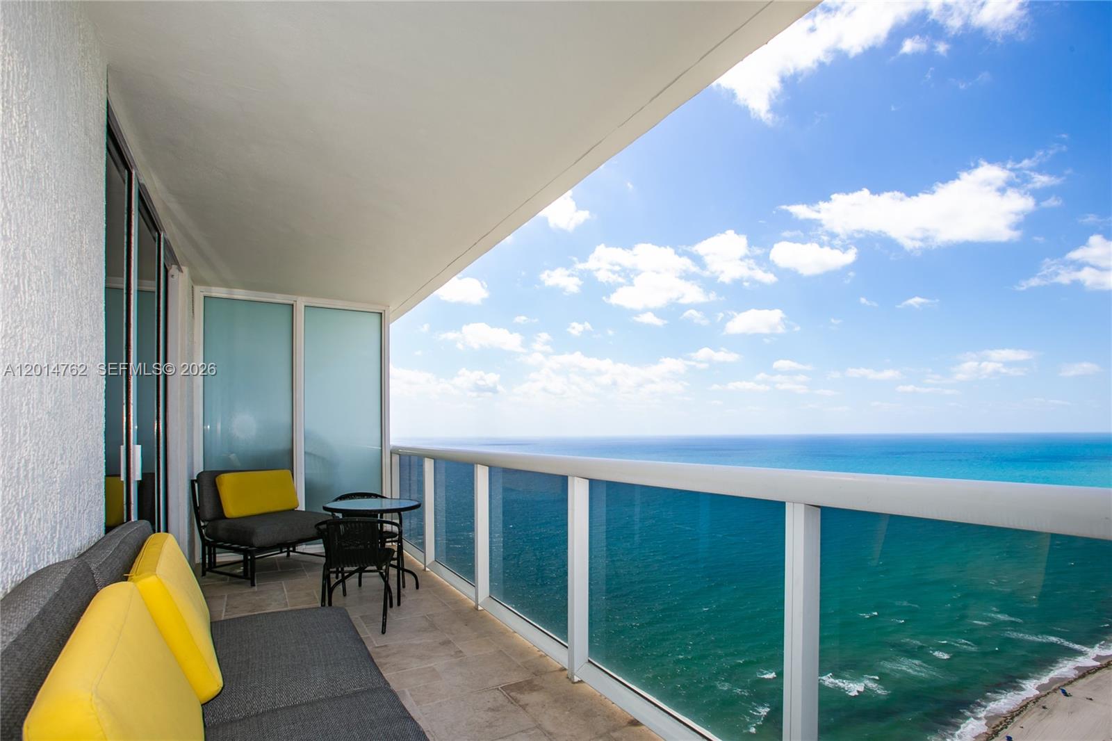 A balcony with outdoor seating overlooks the ocean under a blue sky with clouds — 1830 S Ocean Dr # 4504, Hallandale Beach FL 33009, HALLANDALE BEACH, FL