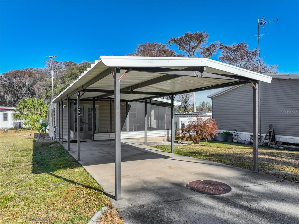 A mobile home features a metal carport covering a concrete driveway and a screened porch — 698 CINDI AVENUE, LEESBURG, FL