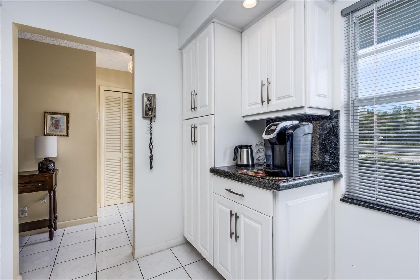 A kitchen corner features white cabinets, dark granite countertops, a coffee maker, and tiled floors — 190 SE 5th Avenue # 108, Dania Beach FL 33004, DANIA BEACH, FL