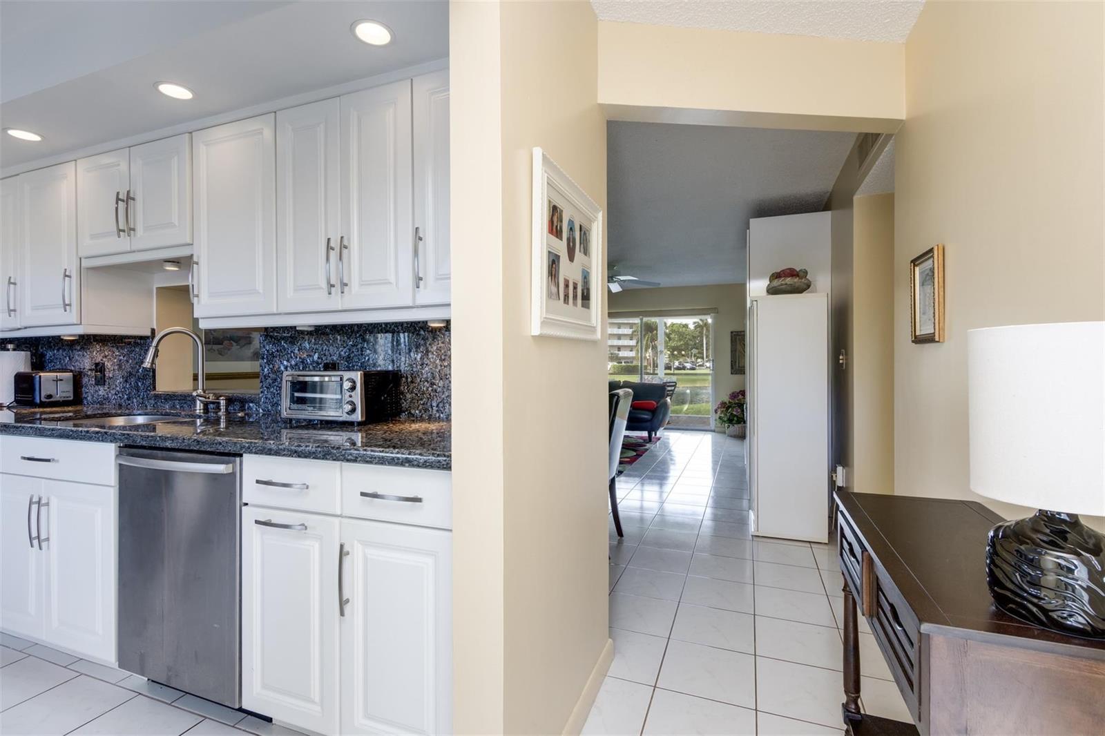 A kitchen with white cabinets and granite countertops opens into a living area with tile floors — 190 SE 5th Avenue # 108, Dania Beach FL 33004, DANIA BEACH, FL