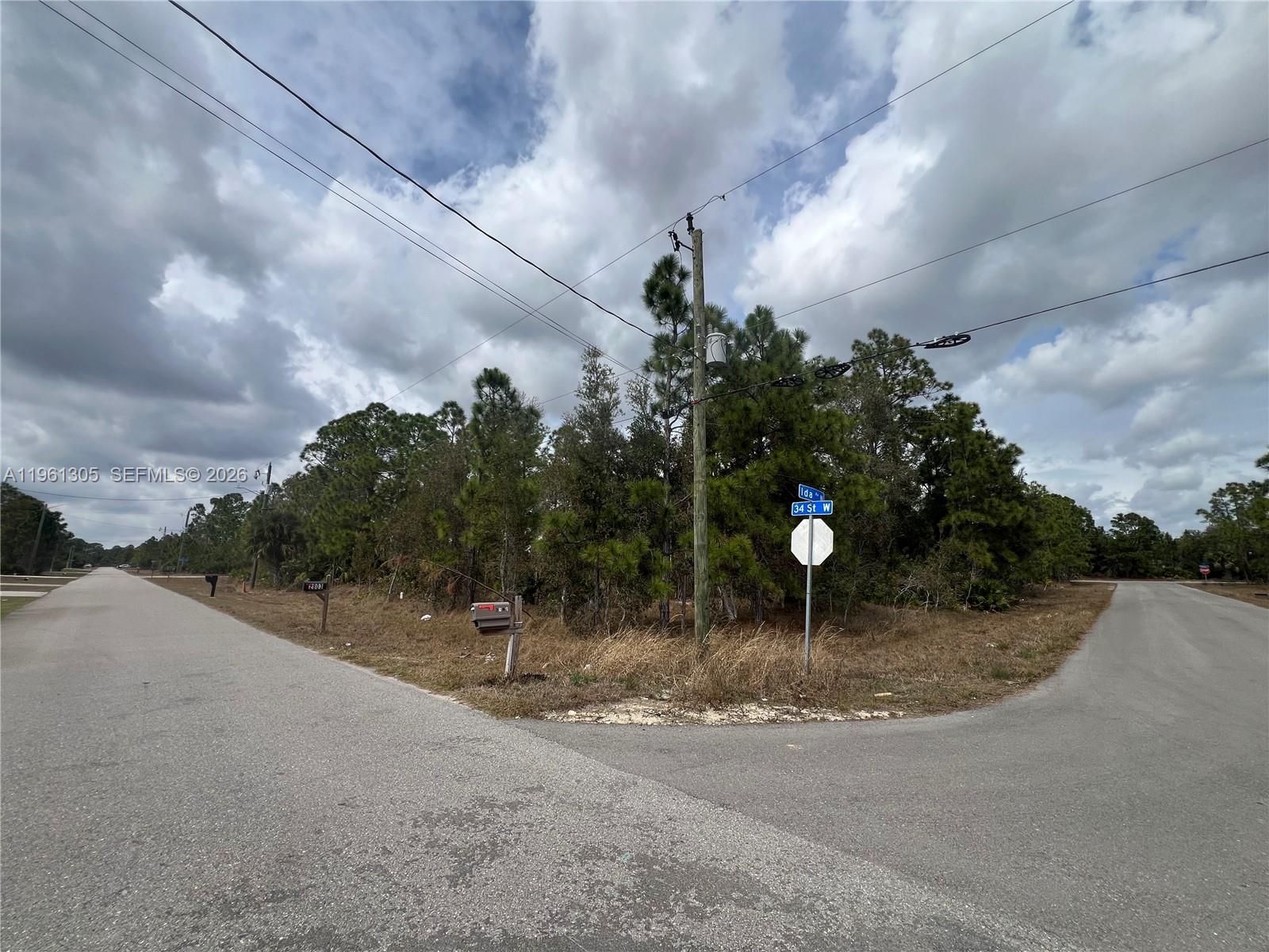A street corner with a utility pole and road signs at a wooded vacant lot — 3400 Irma Ave N, Lehigh Acres FL 33971, LEHIGH ACRES, FL
