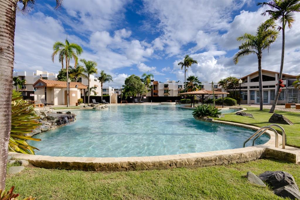 A swimming pool with a stone border, palm trees, and surrounding apartment buildings under a sky — 109 CALLE PLUMOSO REAL UNIT E212, GUAYNABO, PR