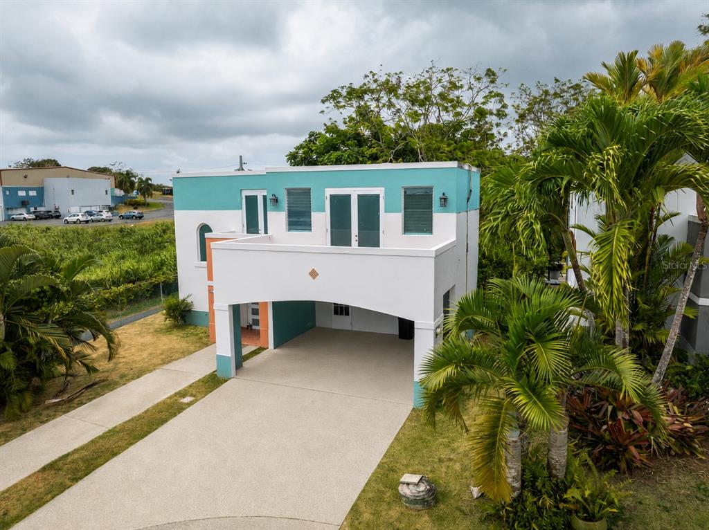 An exterior view of a two-story house with a turquoise and white facade and carport — D-17 URB. VISTA VERDE, FAJARDO, PR