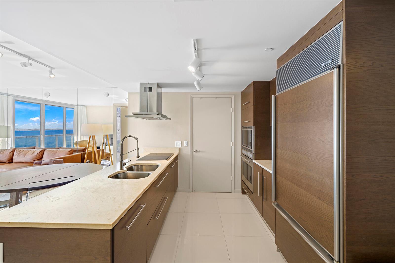 A modern kitchen features wood cabinetry, stainless steel appliances, and a view of the ocean — 495 Brickell Avenue # 911, Miami FL 33131, MIAMI, FL