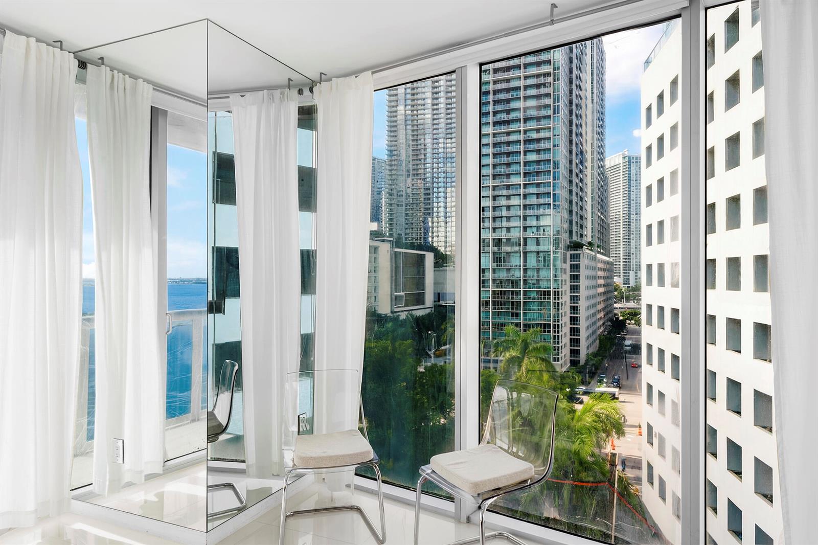 A room with floor-to-ceiling windows, mirrored walls, two clear chairs, and views of city buildings — 495 Brickell Avenue # 911, Miami FL 33131, MIAMI, FL