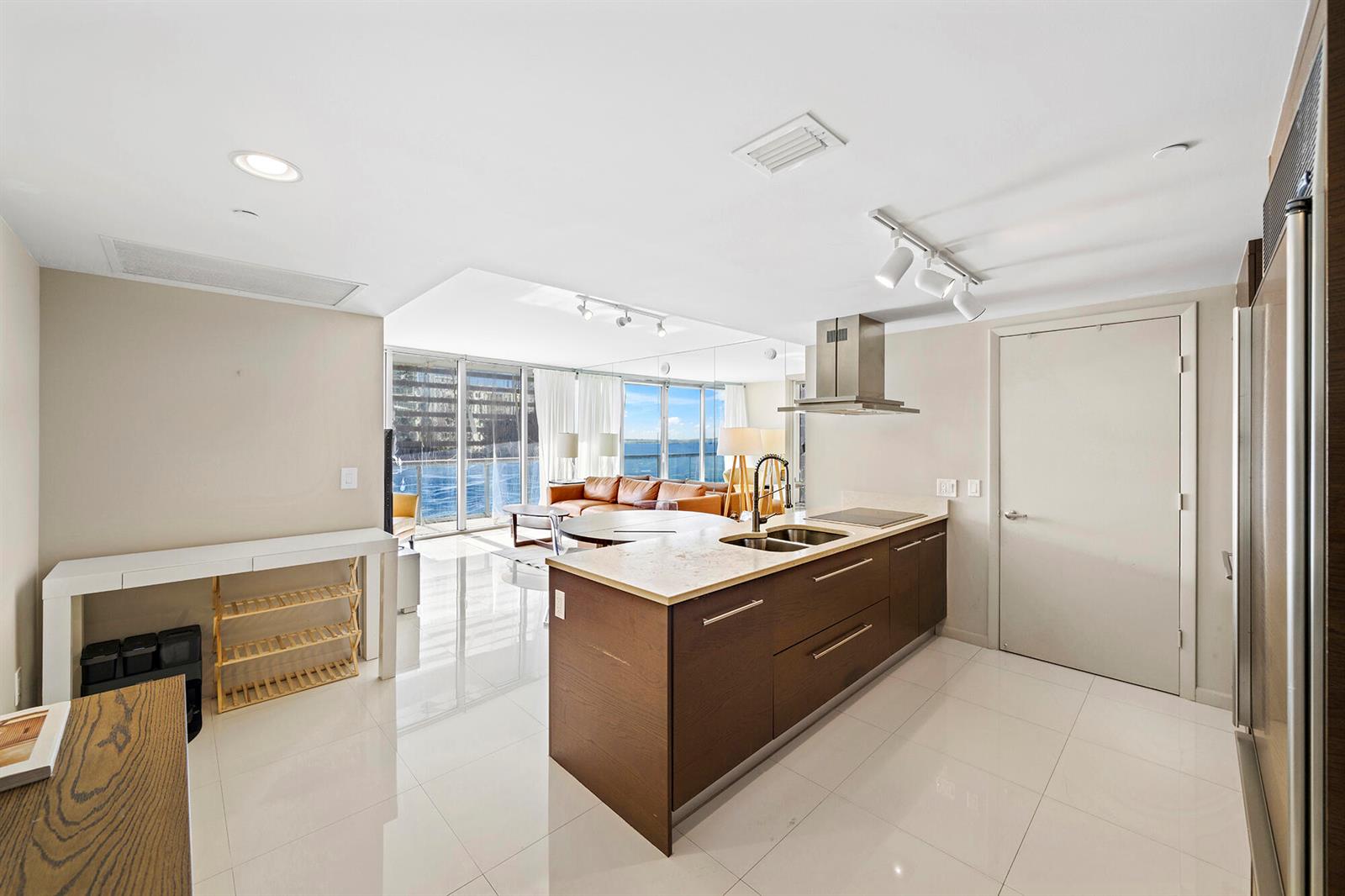 A modern kitchen with a dark wood island and white tile floors overlooks a living area — 495 Brickell Avenue # 911, Miami FL 33131, MIAMI, FL