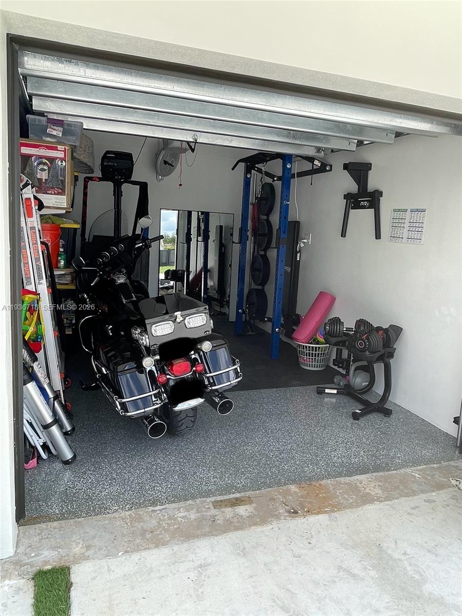 A garage contains a motorcycle, a weight rack, and a dumbbell stand on epoxy flooring — 17831 NW 84th Ct, Miami FL 33015, MIAMI, FL