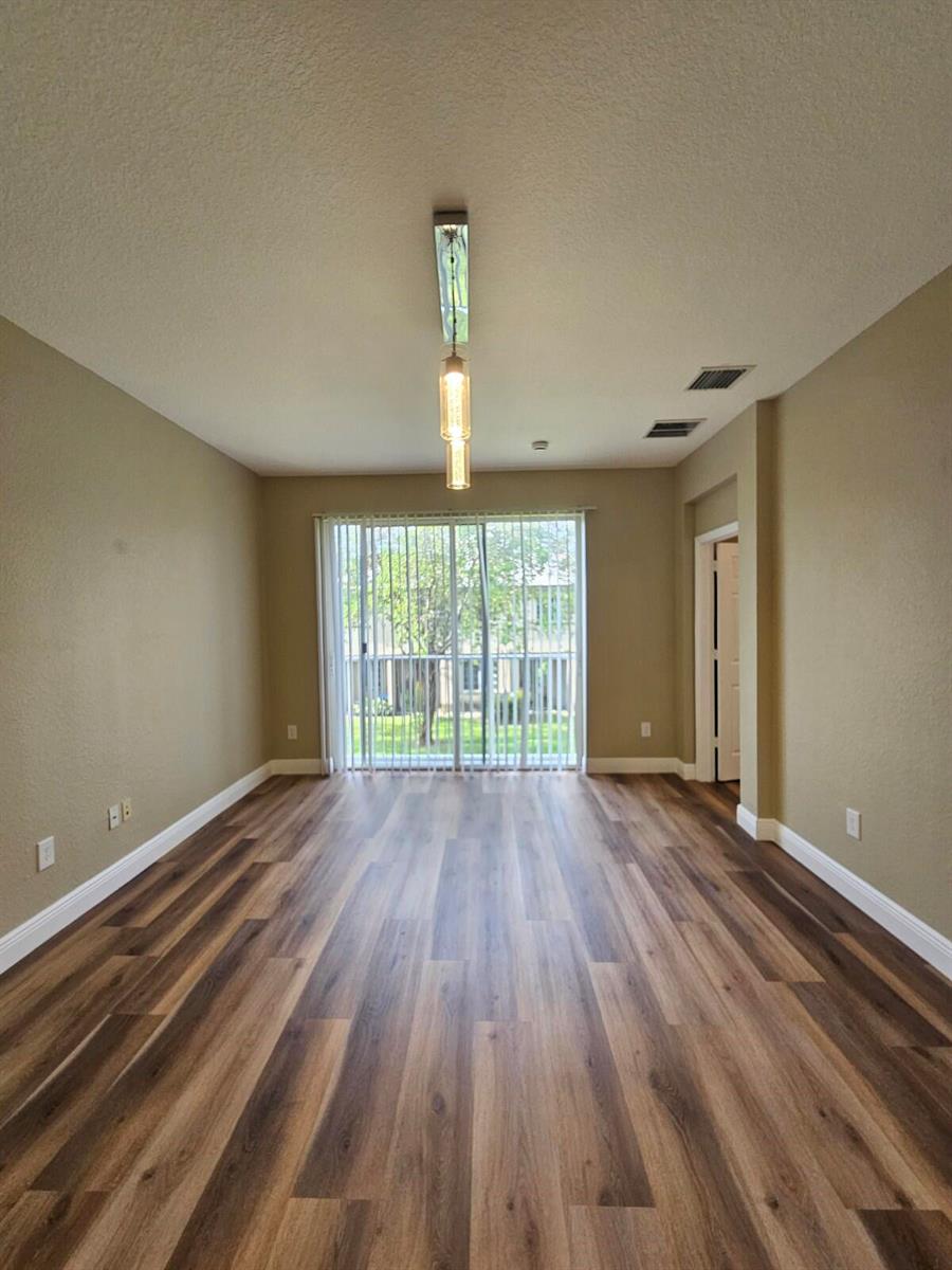 An empty room with wood-look flooring, beige walls, a hanging light fixture, and sliding glass doors — 1967 Freeport Lane, Riviera Beach FL 33404, RIVIERA BEACH, FL