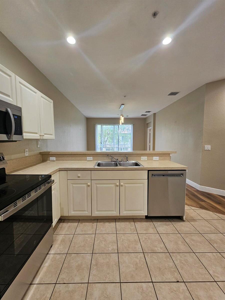 A kitchen features white cabinets, stainless steel appliances, tan countertops, and light-colored tile flooring — 1967 Freeport Lane, Riviera Beach FL 33404, RIVIERA BEACH, FL