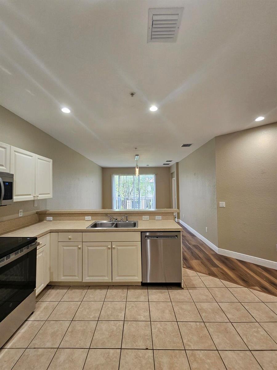 A kitchen with white cabinets, tan countertops, and tile flooring opens to a living area — 1967 Freeport Lane, Riviera Beach FL 33404, RIVIERA BEACH, FL