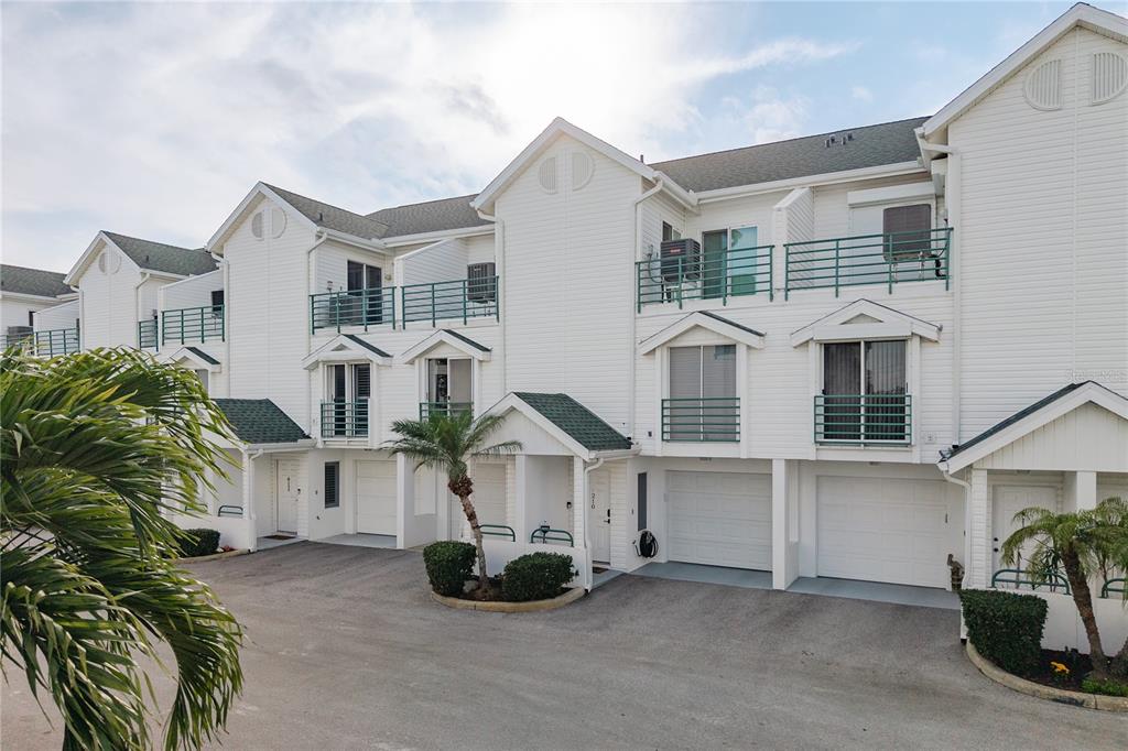 A row of white multi-story townhouses with attached garages and green shingled roof accents — 320 ISLAND WAY UNIT 209, CLEARWATER BEACH, FL
