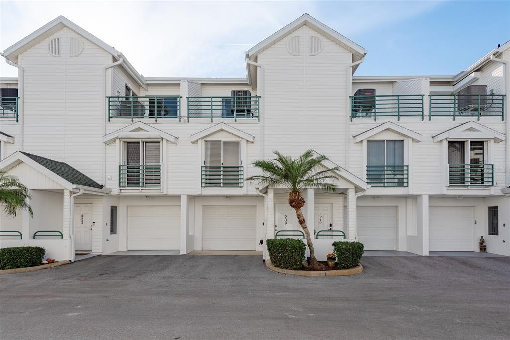 A row of white townhouses features garages, balconies, and a small palm tree in front — 320 ISLAND WAY UNIT 209, CLEARWATER BEACH, FL