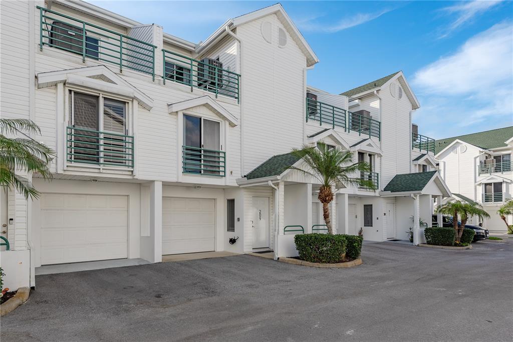 A multi-story white townhouse complex features garages, balconies with green railings, and paved parking — 320 ISLAND WAY UNIT 209, CLEARWATER BEACH, FL