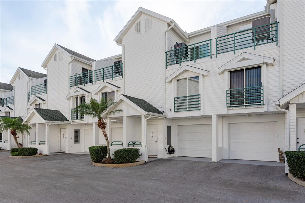 A row of white multi-story townhouses with attached garages and green metal balcony railings — 320 ISLAND WAY UNIT 209, CLEARWATER BEACH, FL