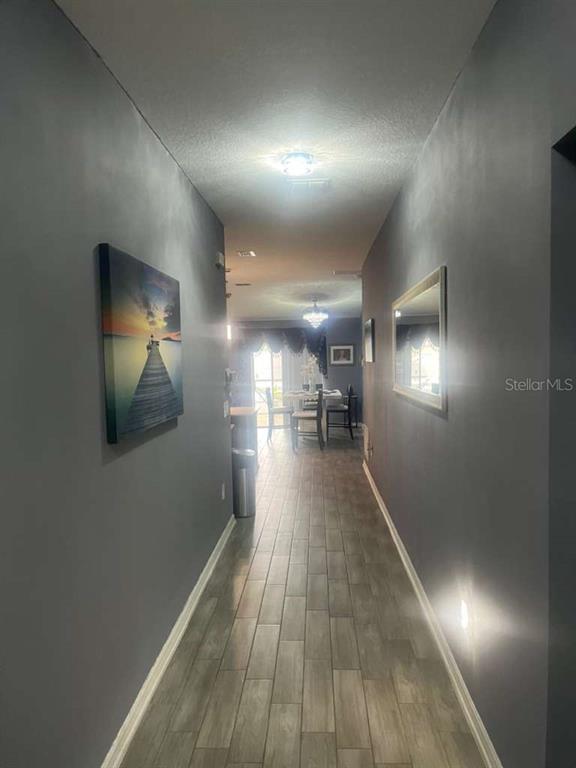 A hallway with gray walls and wood-look tile flooring leads toward a dining area — 815 OFANTO WAY, HAINES CITY, FL