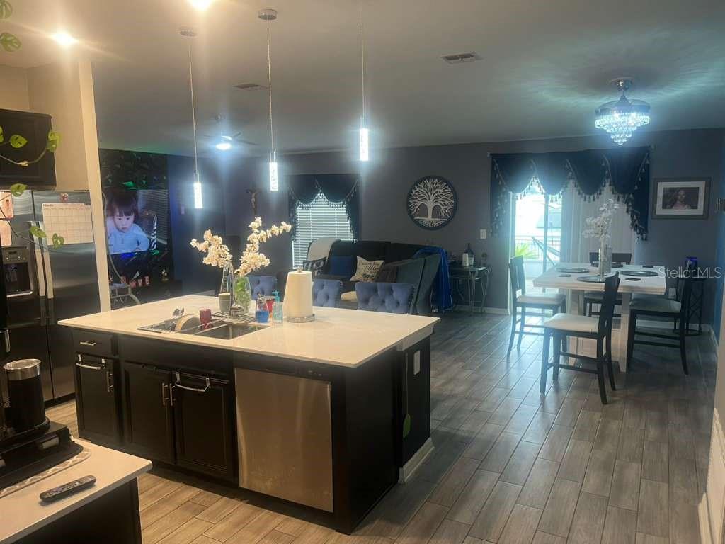 A modern kitchen with a large island and white countertops opens into a dining area — 815 OFANTO WAY, HAINES CITY, FL