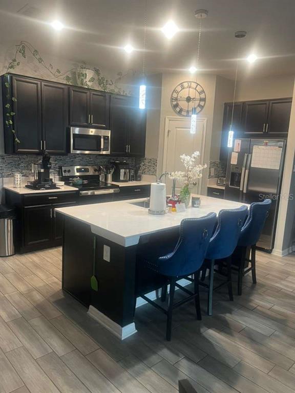 A kitchen features dark cabinets, a white-topped island with blue stools, and stainless appliances — 815 OFANTO WAY, HAINES CITY, FL