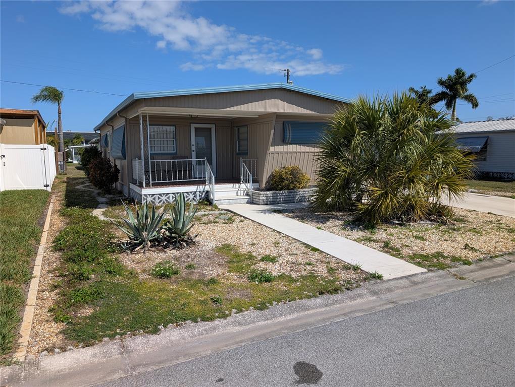 A tan mobile home features a front porch, a concrete walkway, and a palm tree — 107 48TH AVENUE DRIVE W, BRADENTON, FL