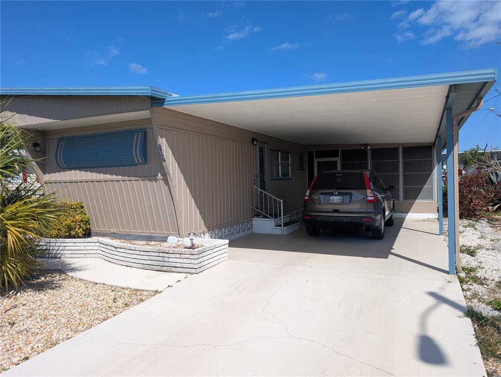 A tan mobile home features a carport, a concrete driveway, and a small brick planter — 107 48TH AVENUE DRIVE W, BRADENTON, FL